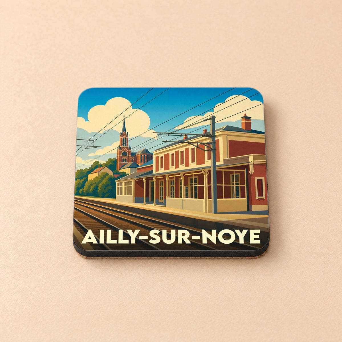 Dessous de verre souvenir de la ville d'Ailly-sur-Noye avec une illustration stylisée de sa gare et de son église.