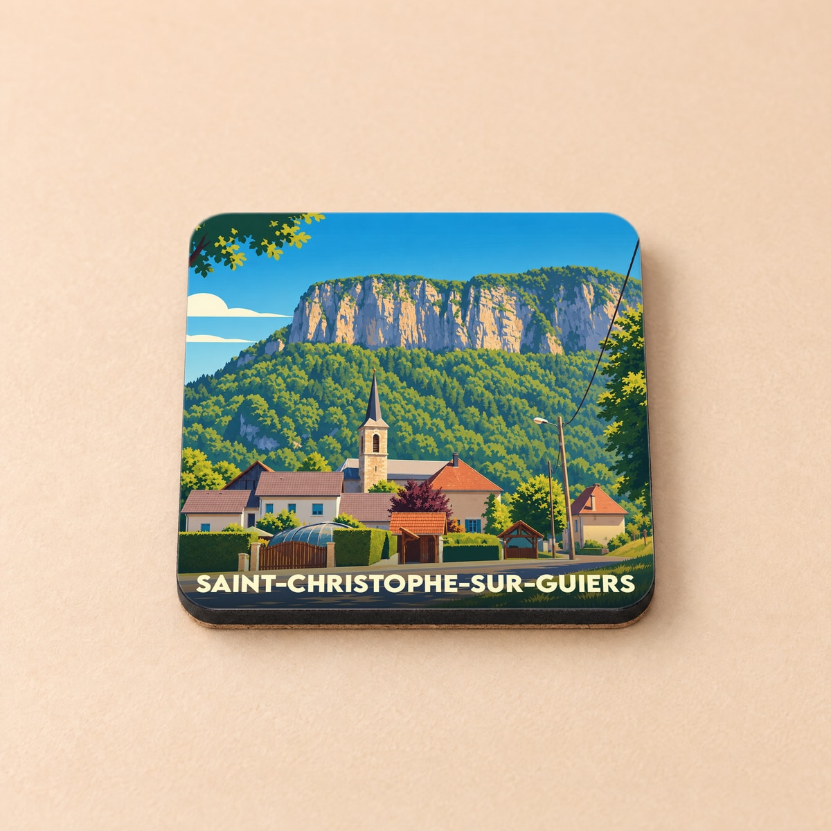 Dessous de verre souvenir de la ville de Saint-Christophe-sur-Guiers avec une illustration stylisée du village et de sa montagne.