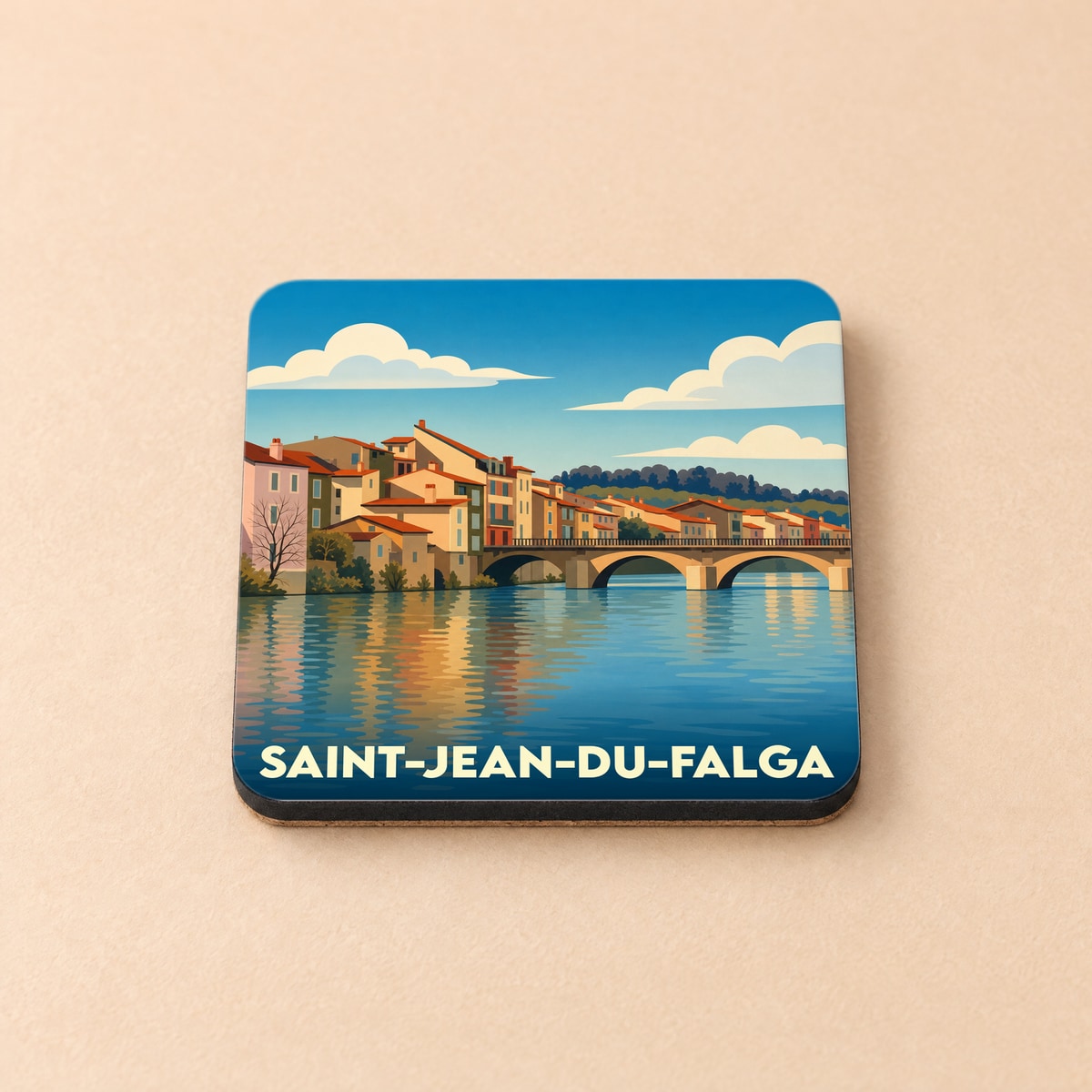 Dessous de verre souvenir de la ville de Saint-Jean-du-Falga avec une illustration stylisée d'un pont et de maisons au bord de l'eau.