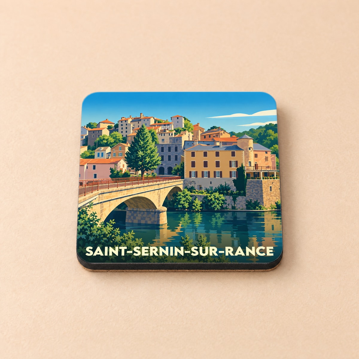Dessous de verre souvenir de la ville de Saint-Sernin-sur-Rance avec une illustration stylisée d'un pont et de maisons colorées.