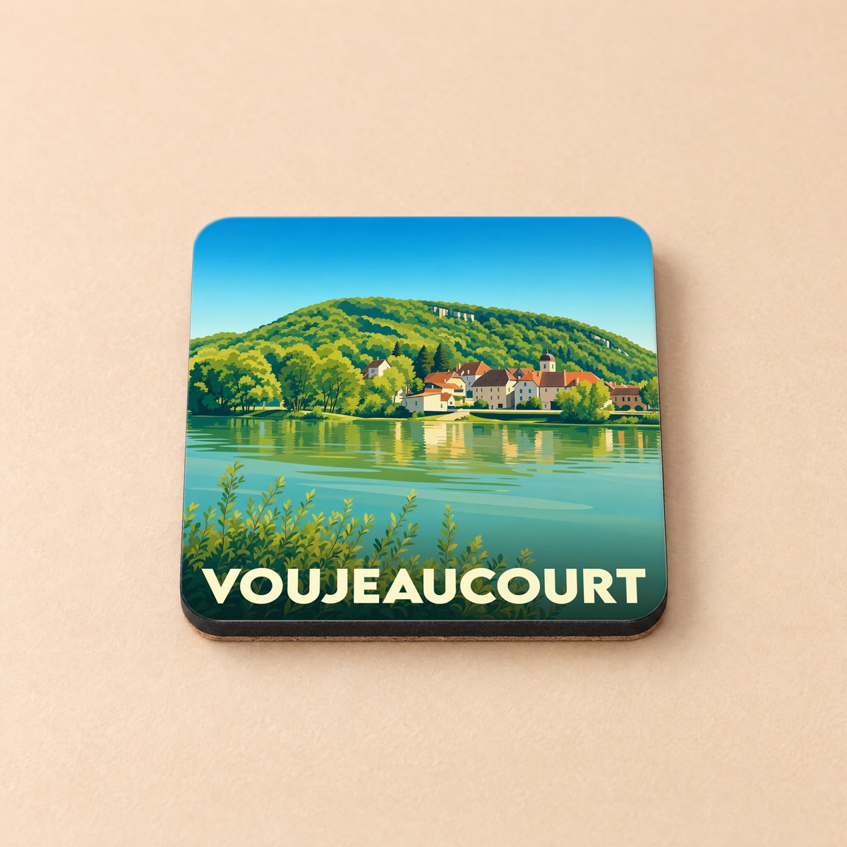Dessous de verre souvenir de la ville de Voujeaucourt avec une illustration stylisée d'un village au bord de l'eau.