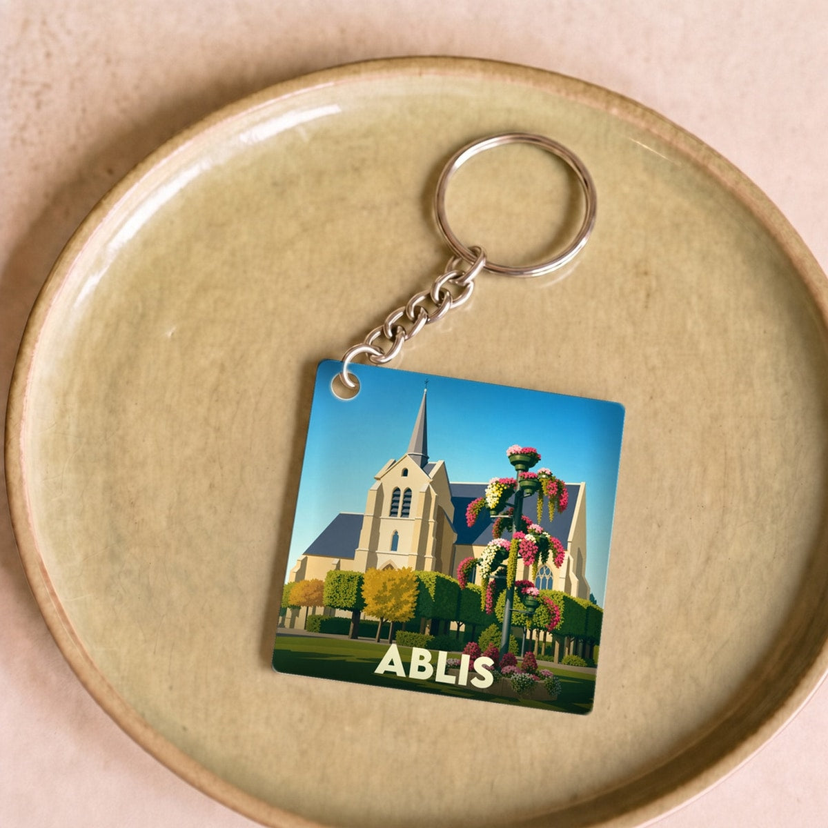 Porte-clés souvenir de la ville d'Ablis avec une illustration stylisée de son église et de jardins fleuris.