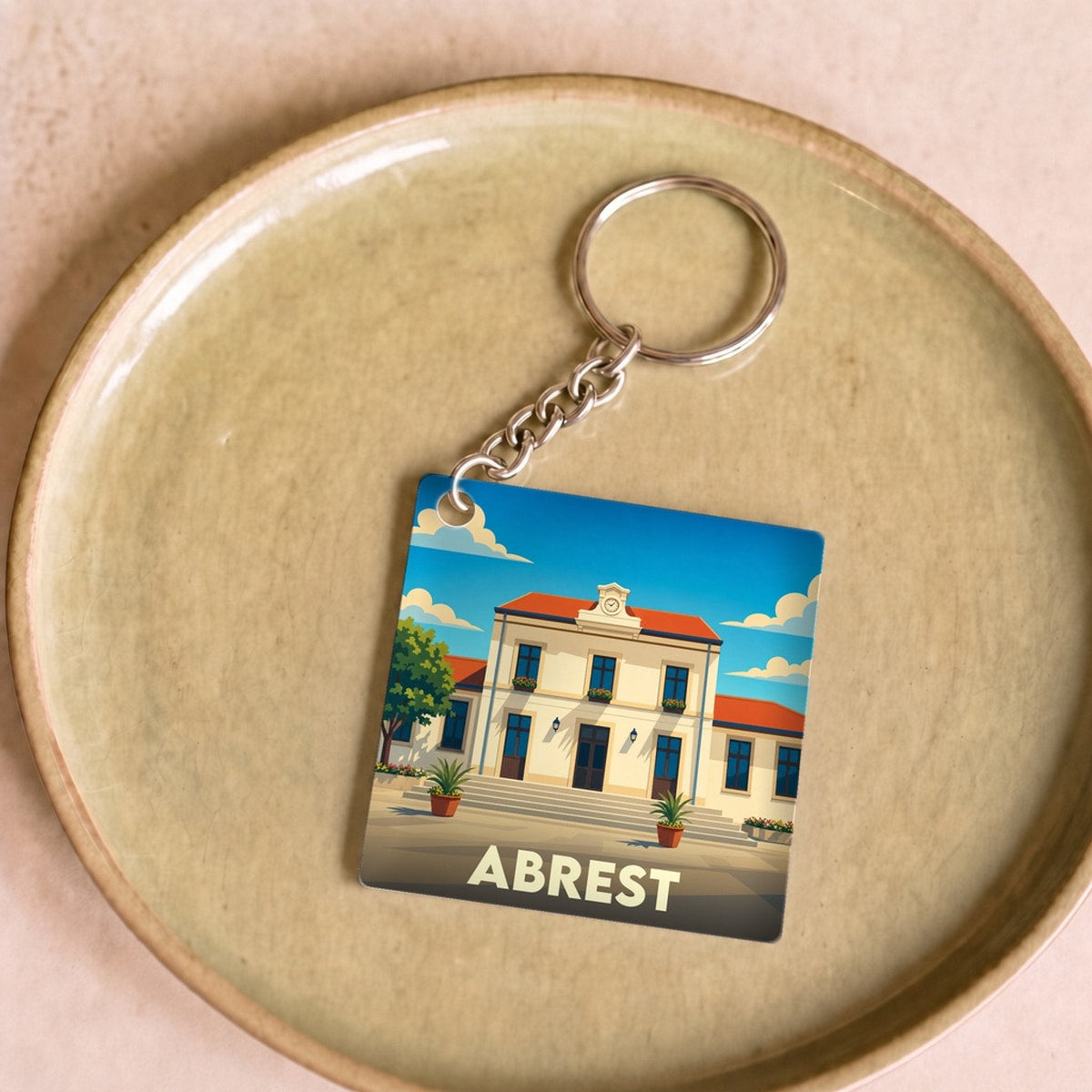 Porte-clés souvenir de la ville d'Abrest avec une illustration stylisée de sa mairie sous un ciel bleu.