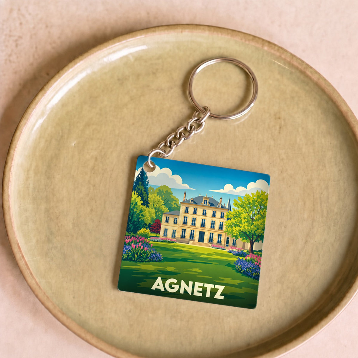 Porte-clés souvenir de la ville d'Agnetz avec une illustration stylisée d'un manoir et de son jardin.