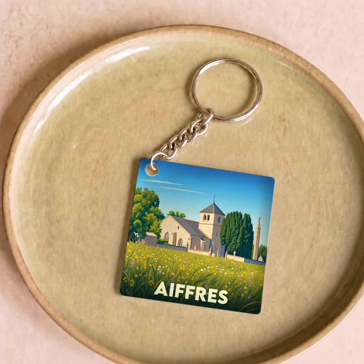 Porte-clés souvenir de la ville d'Aiffres avec une illustration stylisée de son église dans un champ fleuri.