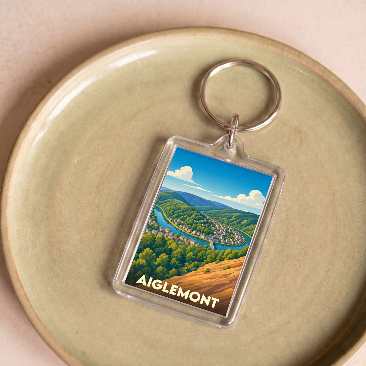 Porte-clés souvenir de la ville d'Aiglemont avec une illustration stylisée d'un paysage de vallée.
