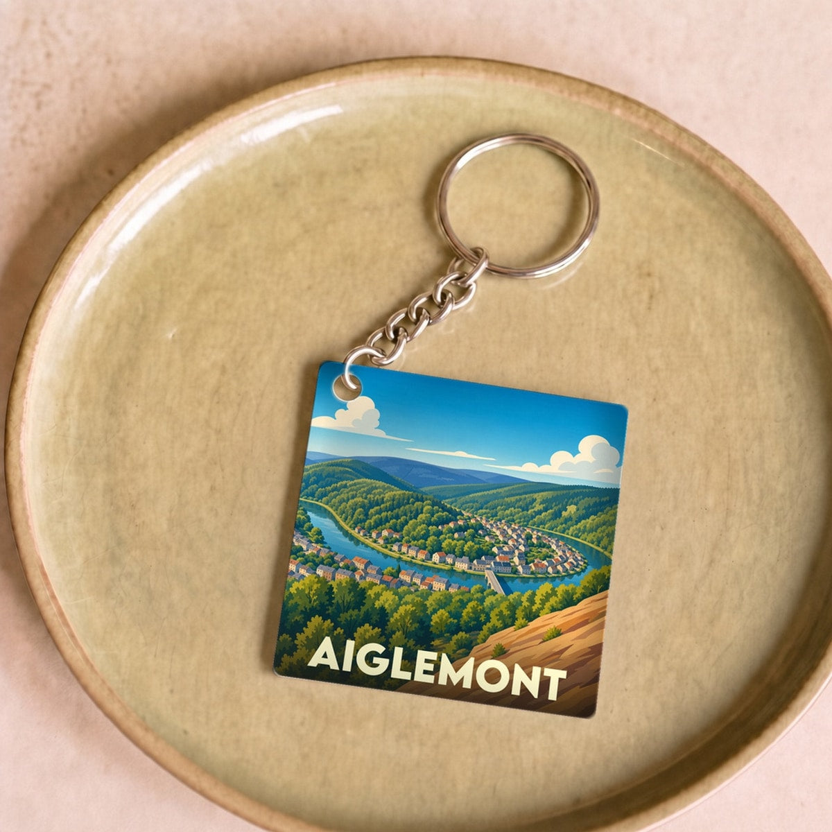 Porte-clés souvenir de la ville d'Aiglemont avec une illustration stylisée d'un paysage de vallée.