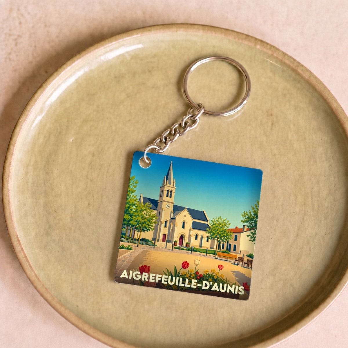 Porte-clés souvenir de la ville d'Aigrefeuille-d'Aunis avec une illustration stylisée de son église et de fleurs colorées.