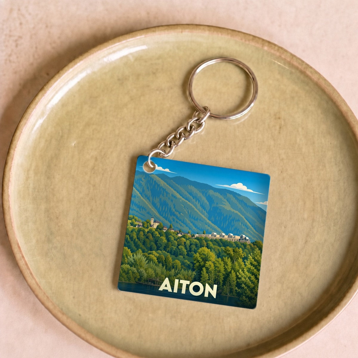 Porte-clés souvenir de la ville d'Aiton avec une illustration stylisée de paysages montagneux.