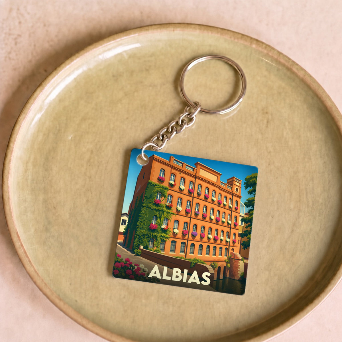 Porte-clés souvenir de la ville d'Albias avec une illustration stylisée d'un bâtiment fleuri.