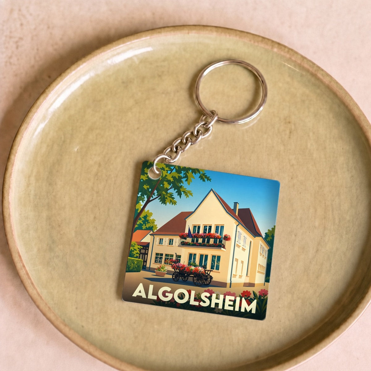 Porte-clés souvenir de la ville d'Algolsheim avec une illustration stylisée d'une maison fleurie.