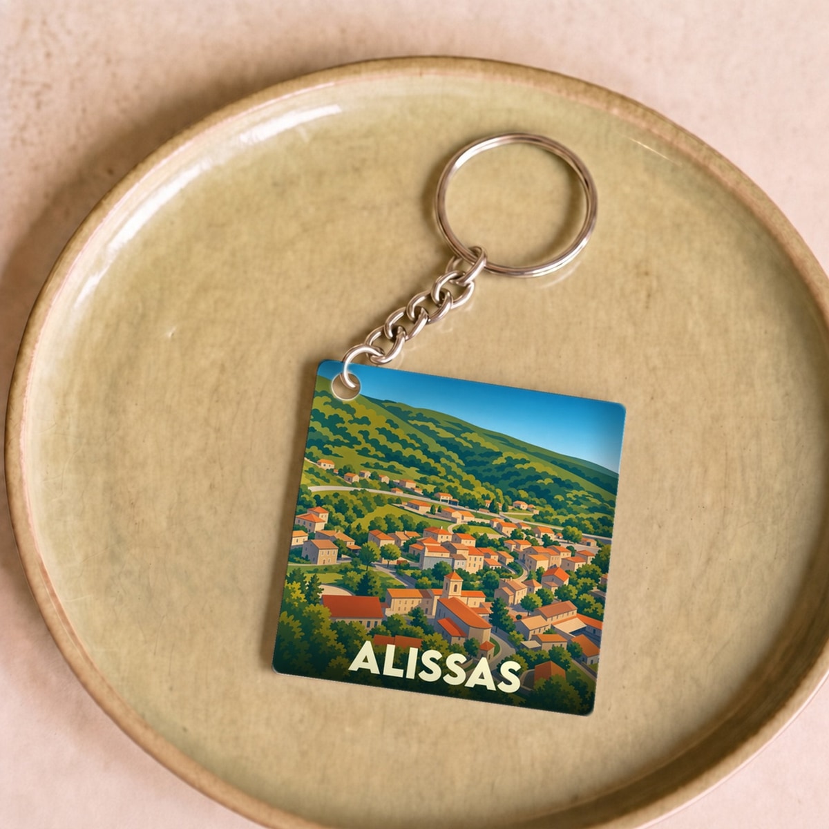 Porte-clés souvenir de la ville d'Alissas avec une illustration stylisée d'un village niché dans des collines verdoyantes.