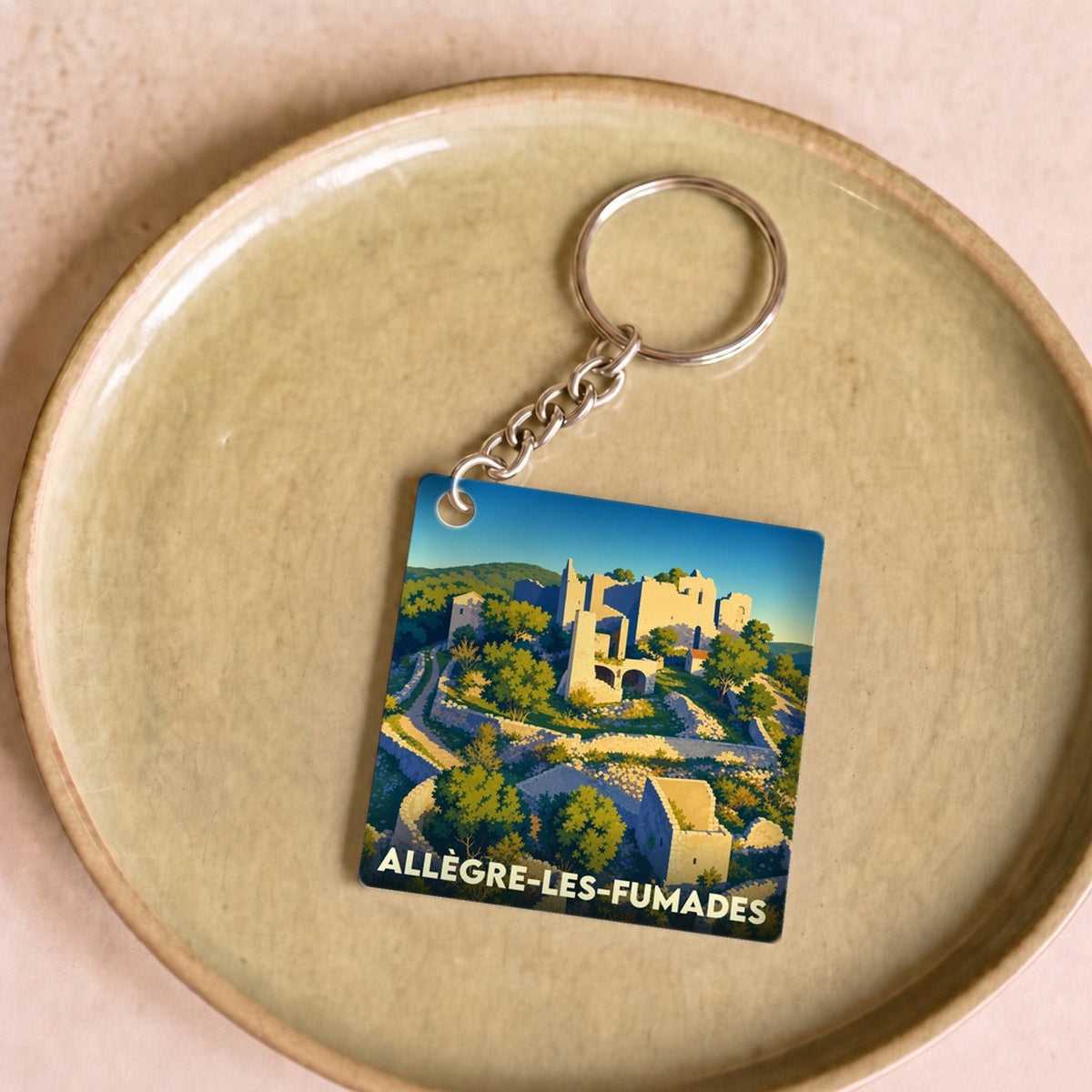 Porte-clés souvenir de la ville d'Allègre-les-Fumades avec une illustration stylisée de son patrimoine.