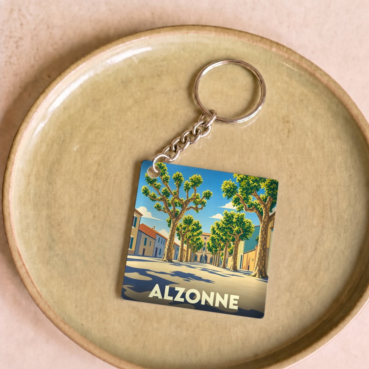 Porte-clés souvenir de la ville d'Alzonne avec une illustration stylisée d'une rue bordée de platanes.