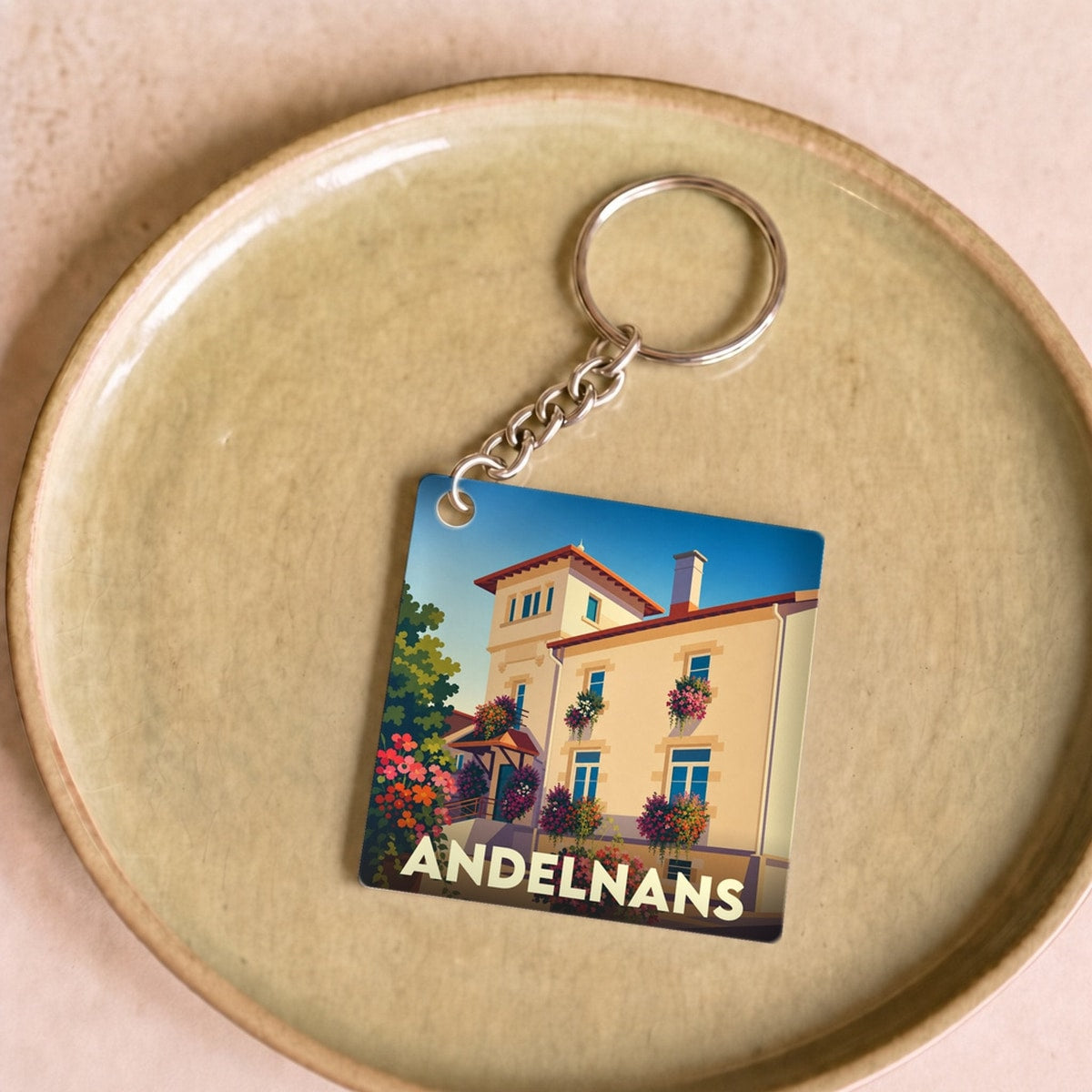 Porte-clés souvenir de la ville d'Andelnans avec une illustration stylisée d'un bâtiment fleuri.