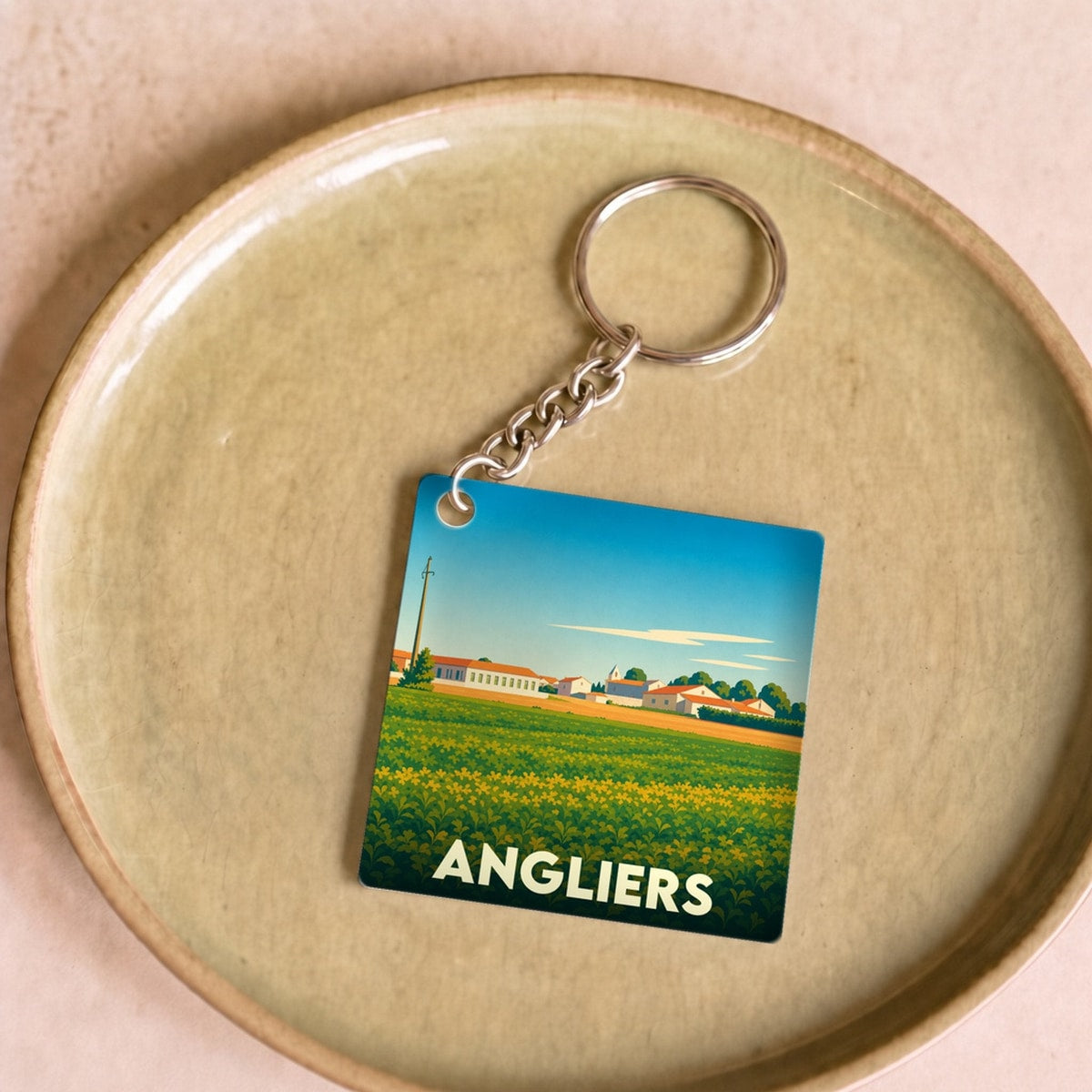 Porte-clés souvenir de la ville d'Angliers avec une illustration stylisée d'un paysage champêtre.