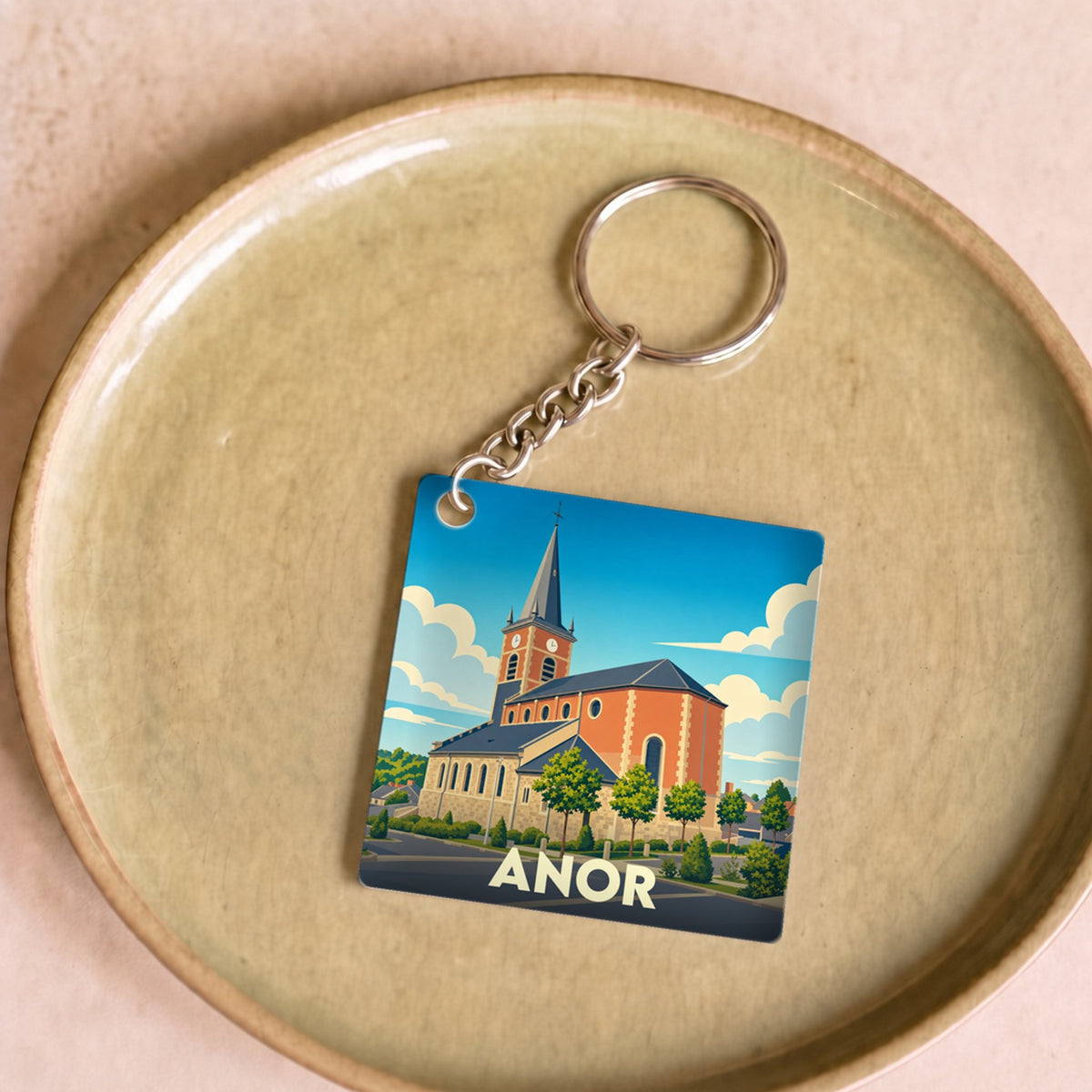Porte-clés souvenir de la ville d'Anor avec une illustration stylisée de son église.