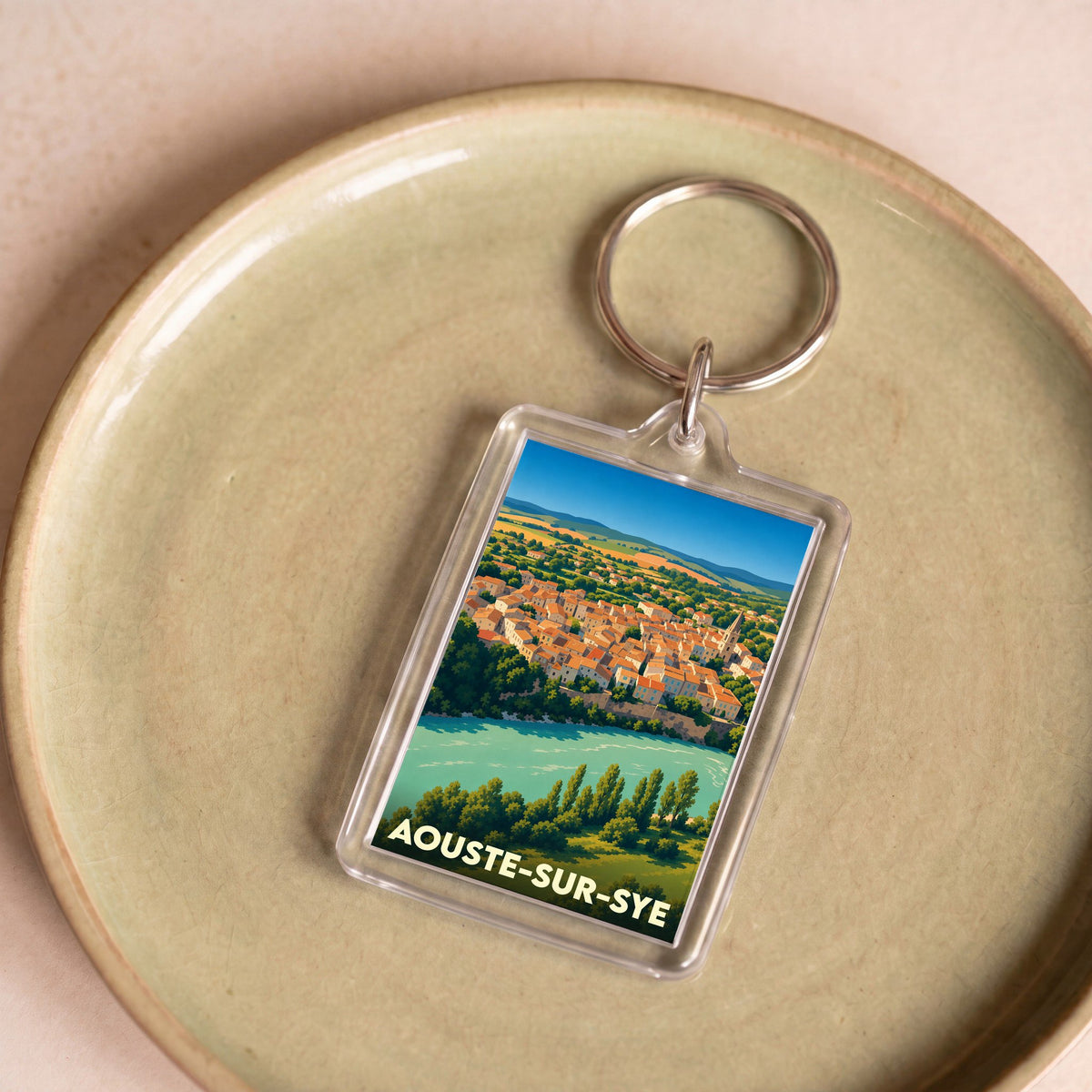 Porte-clés souvenir de la ville de Aouste-sur-Sye avec une illustration colorée et stylisée du village en bord de rivière.