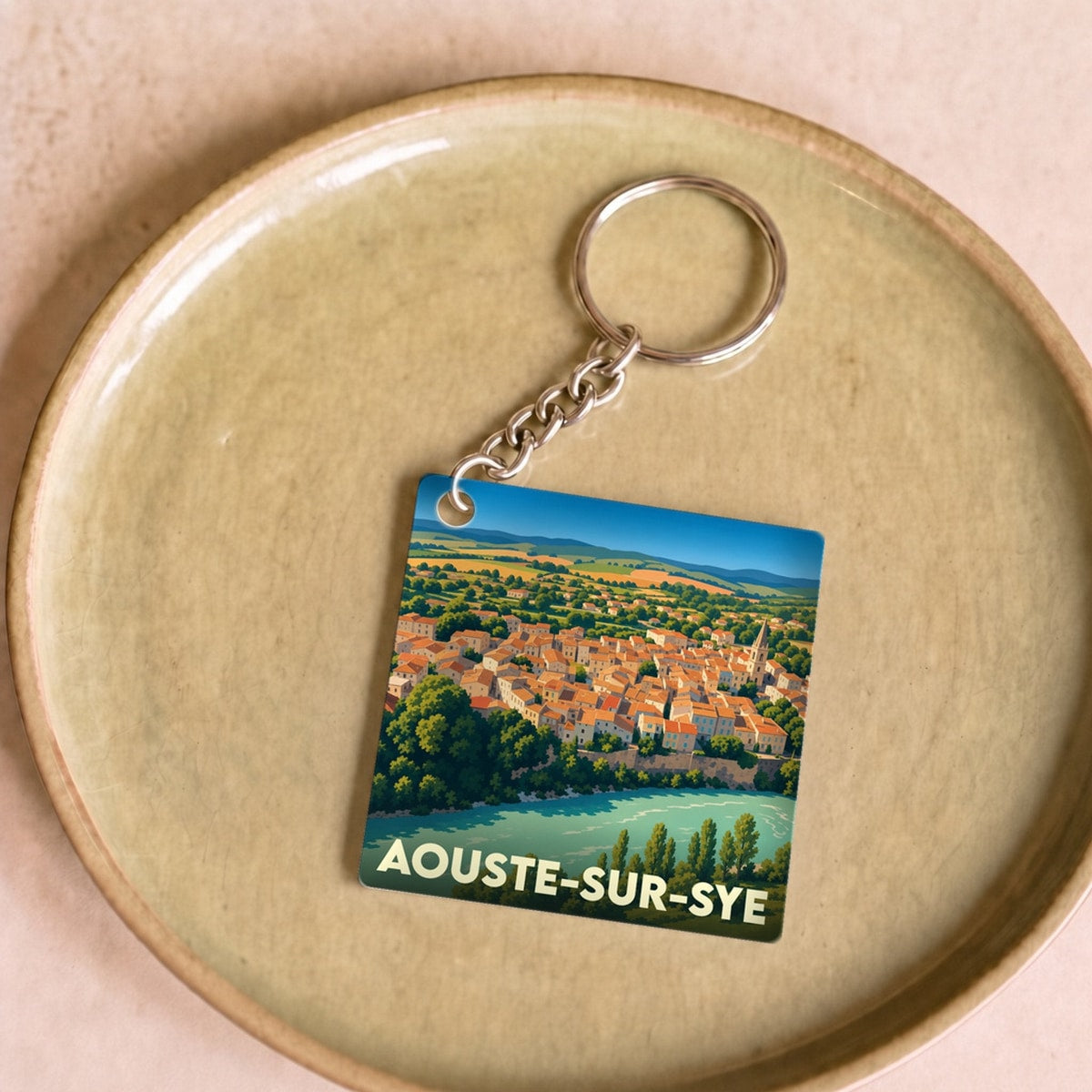 Porte-clés souvenir de la ville de Aouste-sur-Sye avec une illustration colorée et stylisée du village en bord de rivière.