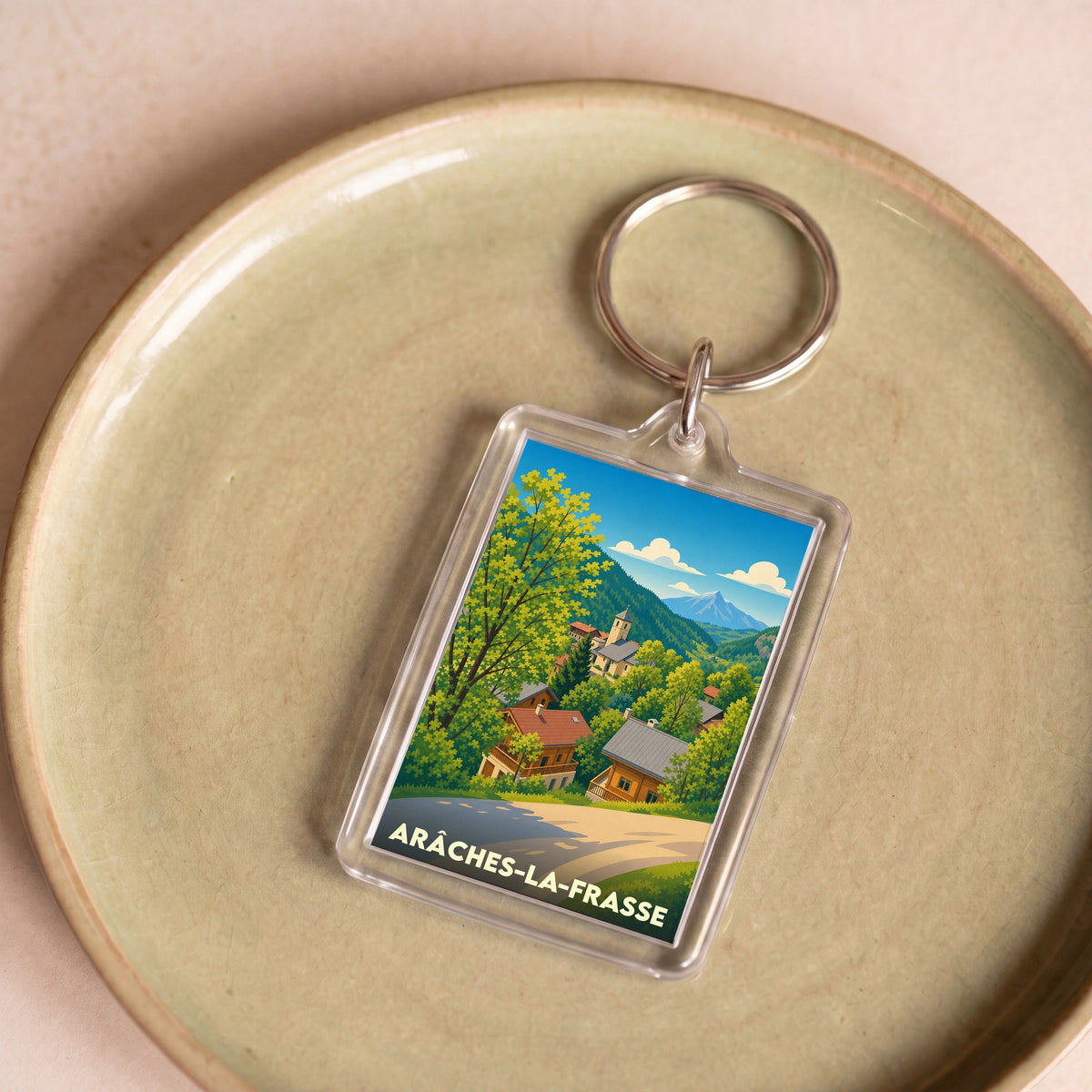 Porte-clés souvenir de la ville d'Arâches-la-Frasse avec une illustration stylisée d'un village de montagne.