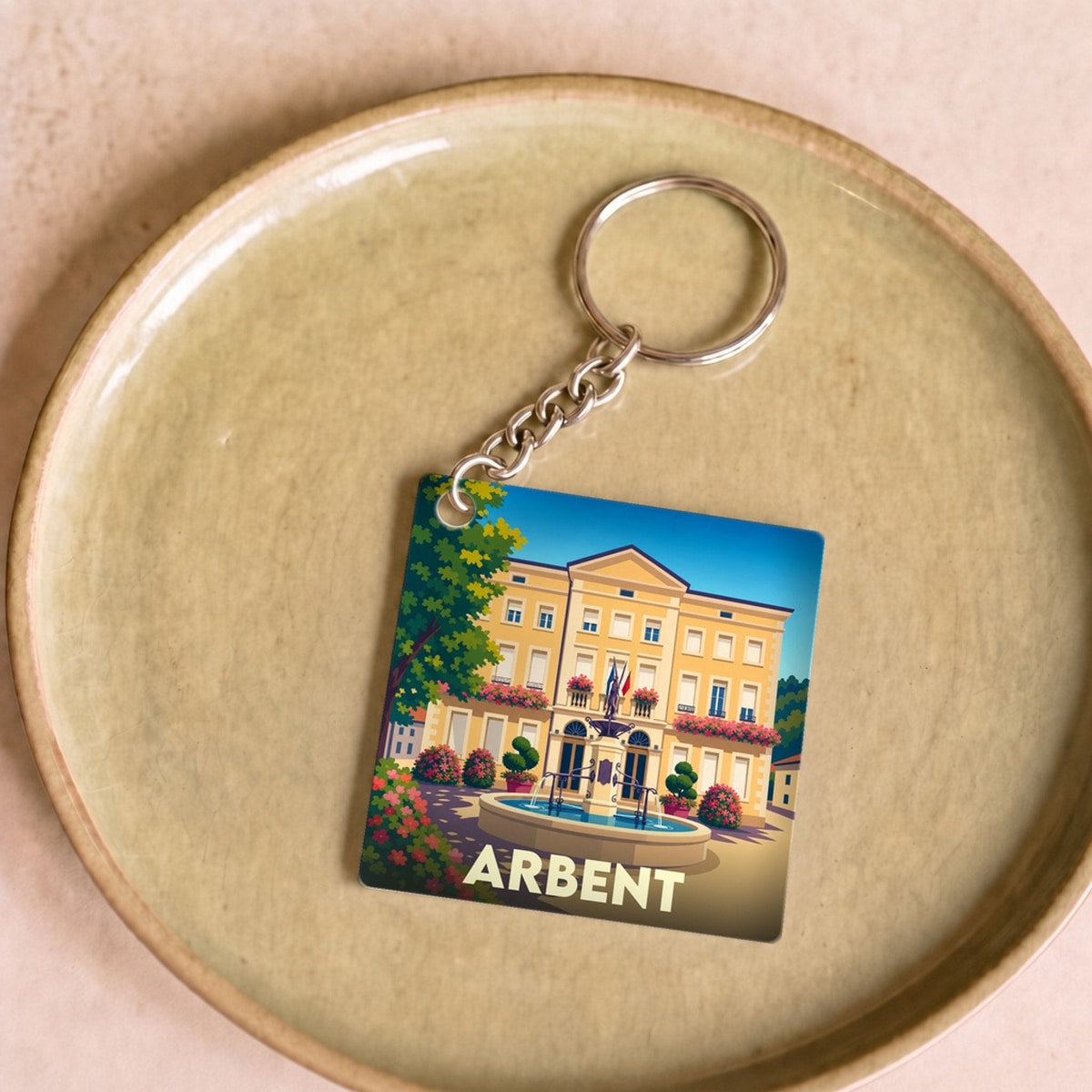 Porte-clés souvenir de la ville d'Arbent avec une illustration stylisée de sa mairie et d'une fontaine.