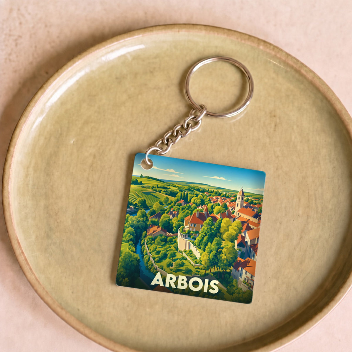 Porte-clés souvenir de la ville d'Arbois avec une illustration colorée de ses paysages et de son architecture.