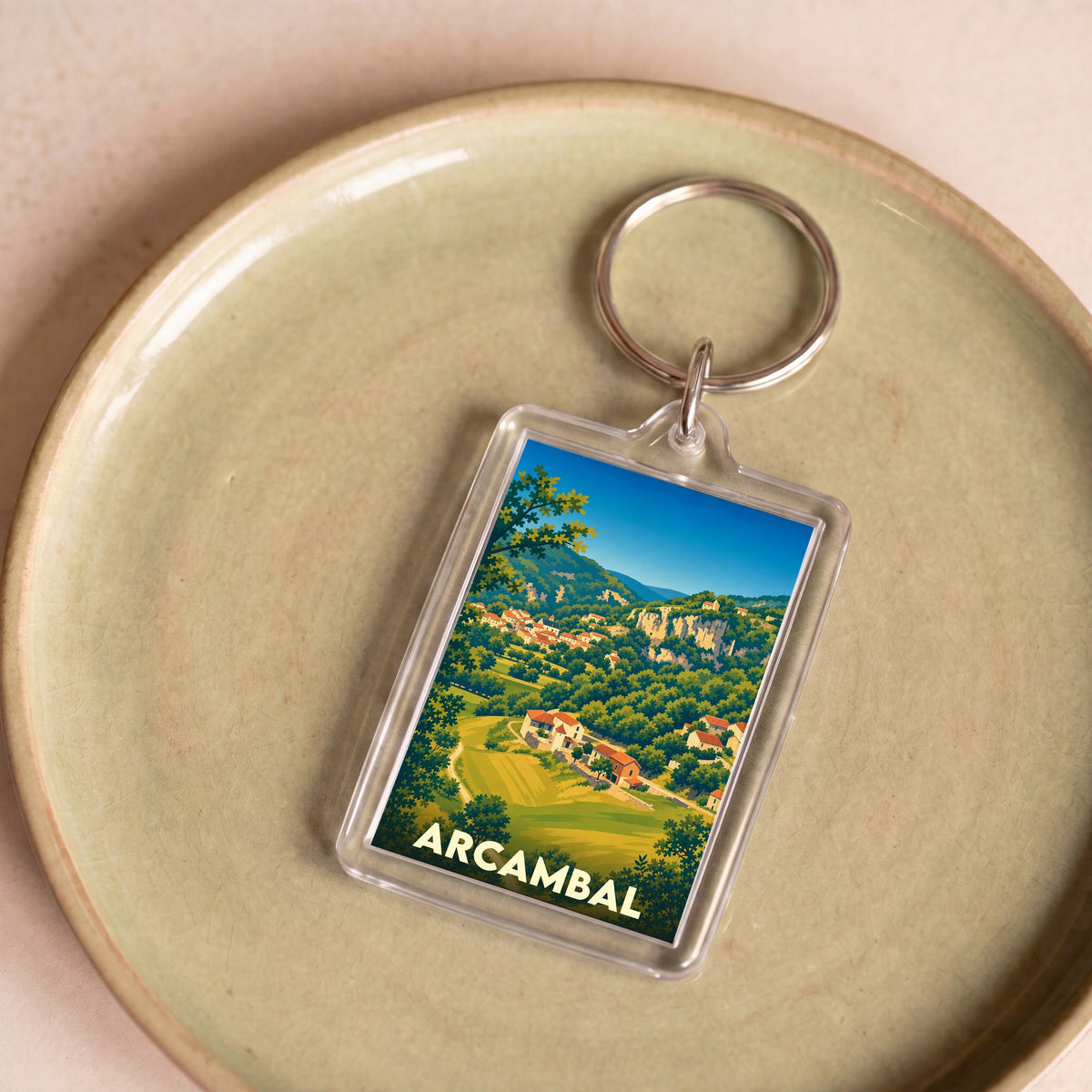 Porte-clés souvenir de la ville de Arcambal avec une illustration stylisée de son paysage vallonné.