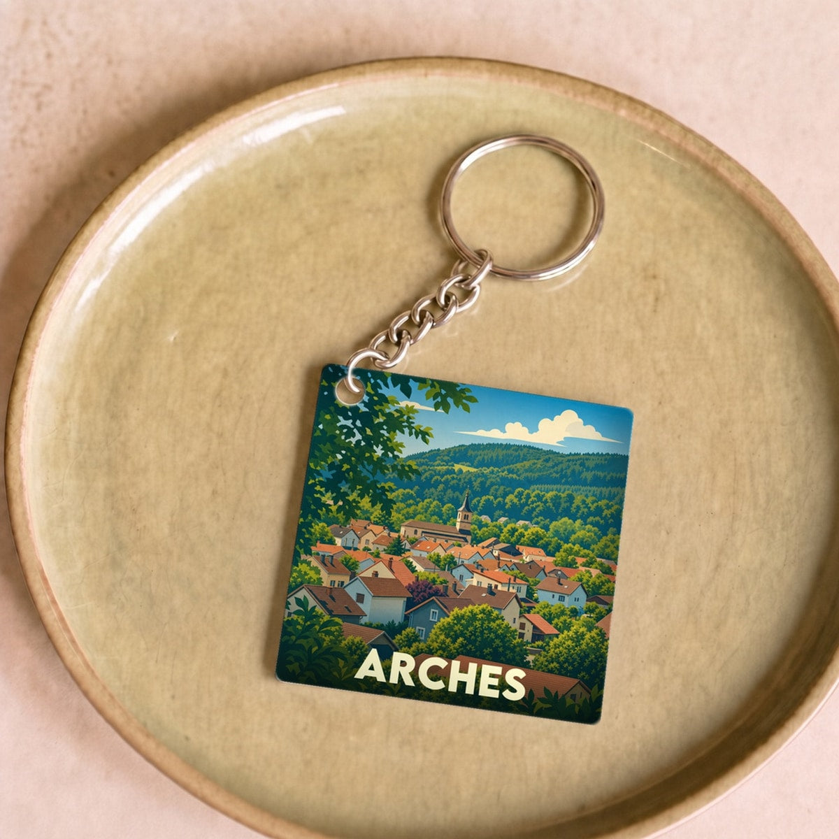 Porte-clés souvenir de la ville d'Arches avec une illustration stylisée de son paysage urbain niché dans la verdure.