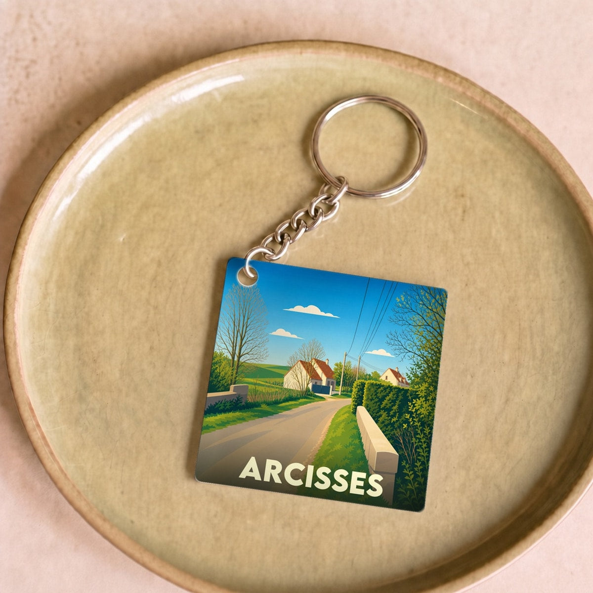 Porte-clés souvenir de la ville de Arcisses avec une illustration stylisée de paysage rural.