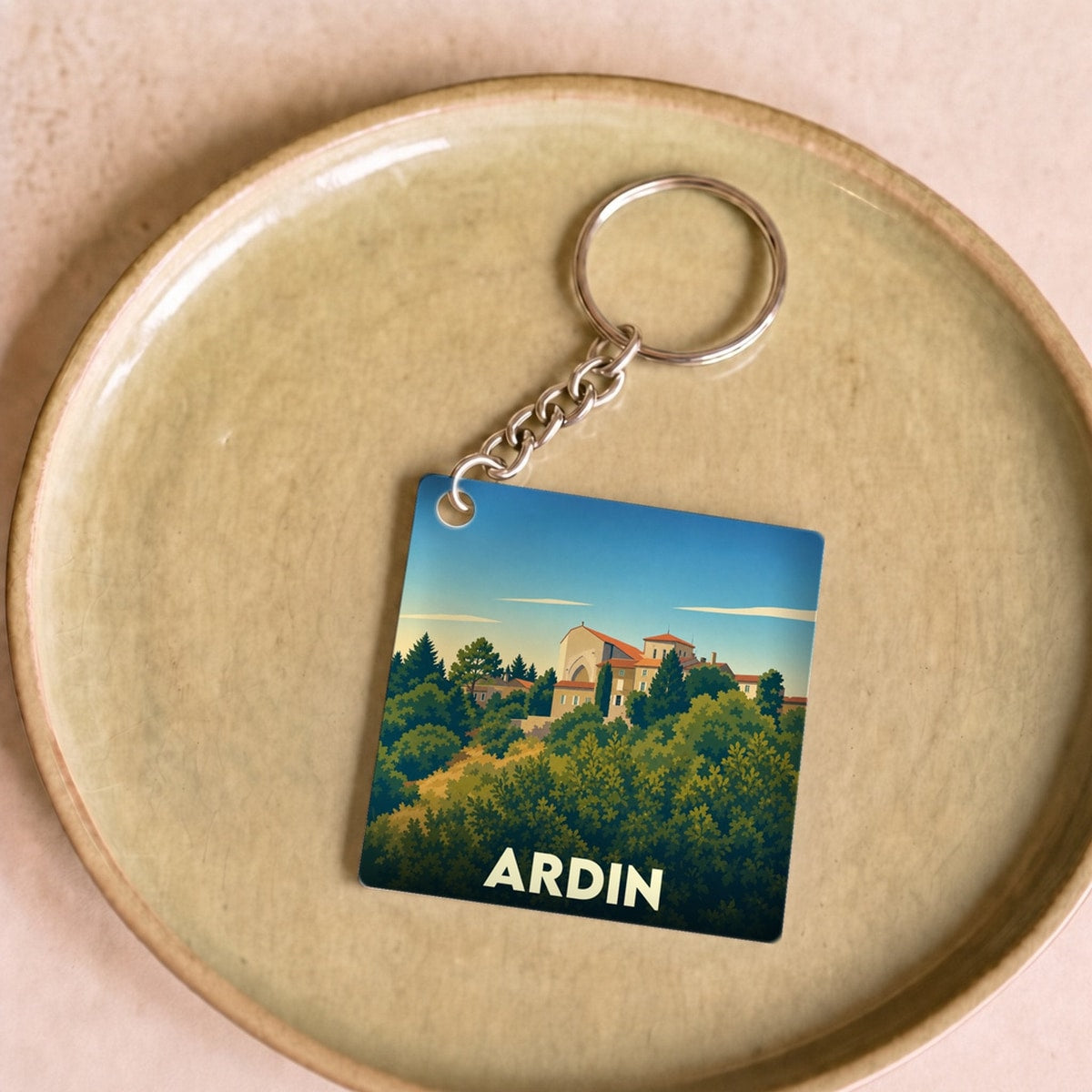 Porte-clés souvenir de la ville d'Ardin avec une illustration stylisée d'un paysage arboré et d'un bâtiment ancien.