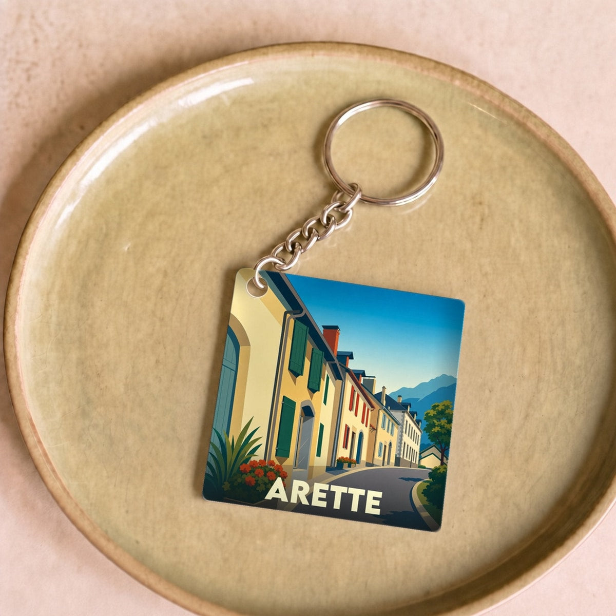 Porte-clés souvenir de la ville d'Arette avec une illustration stylisée d'une rue pittoresque.