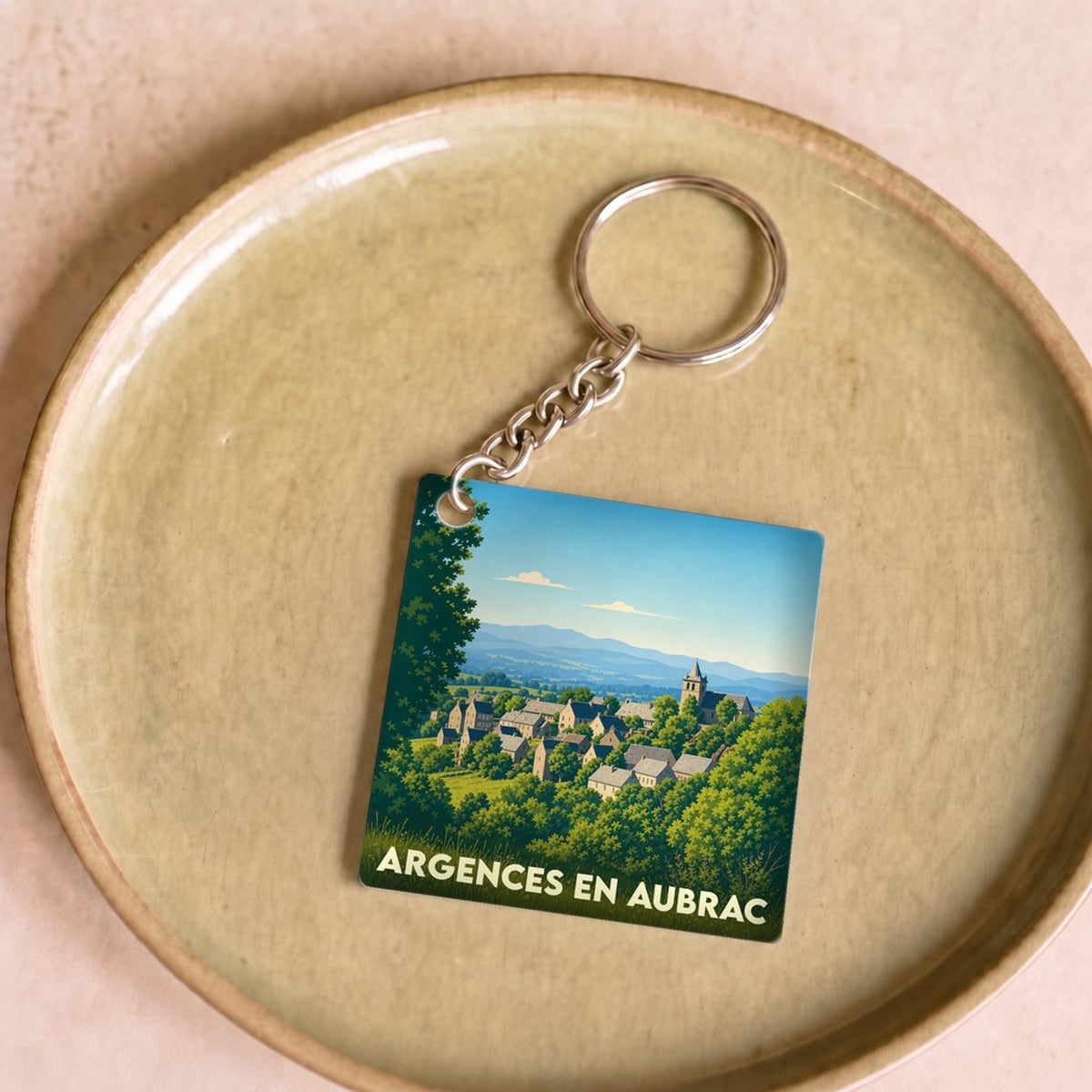 Porte-clés souvenir d'Argences en Aubrac avec une illustration stylisée d'un village niché dans la verdure.