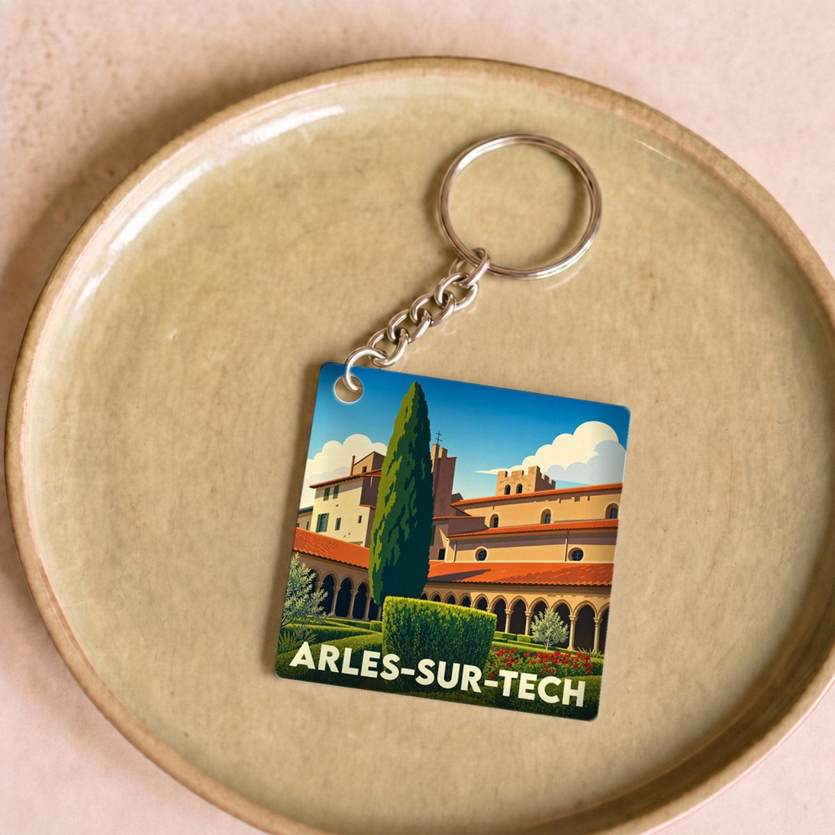 Porte-clés souvenir de la ville d'Arles-sur-Tech avec une illustration stylisée d'un cloître et de jardins.