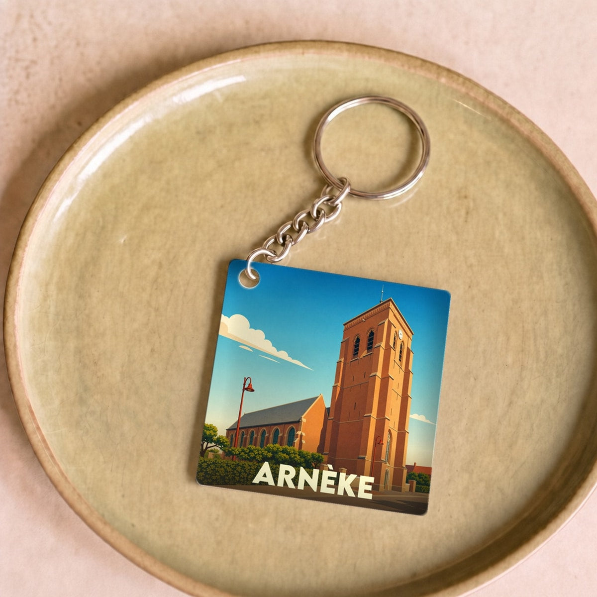 Porte-clés souvenir de la ville d'Arnèke avec une illustration stylisée de son église.