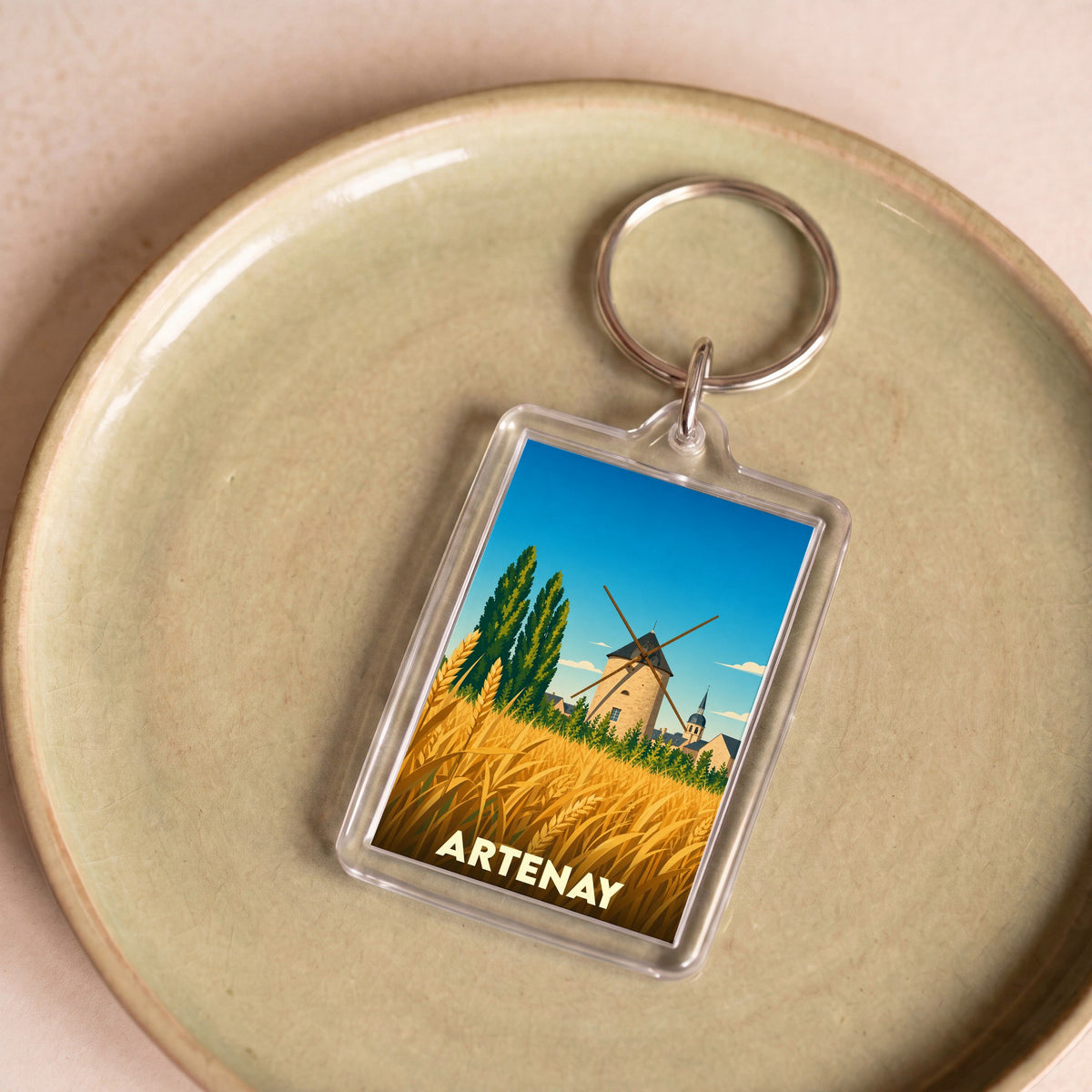 Porte-clés souvenir de la ville d'Artenay avec une illustration stylisée d'un moulin et d'un champ de blé.