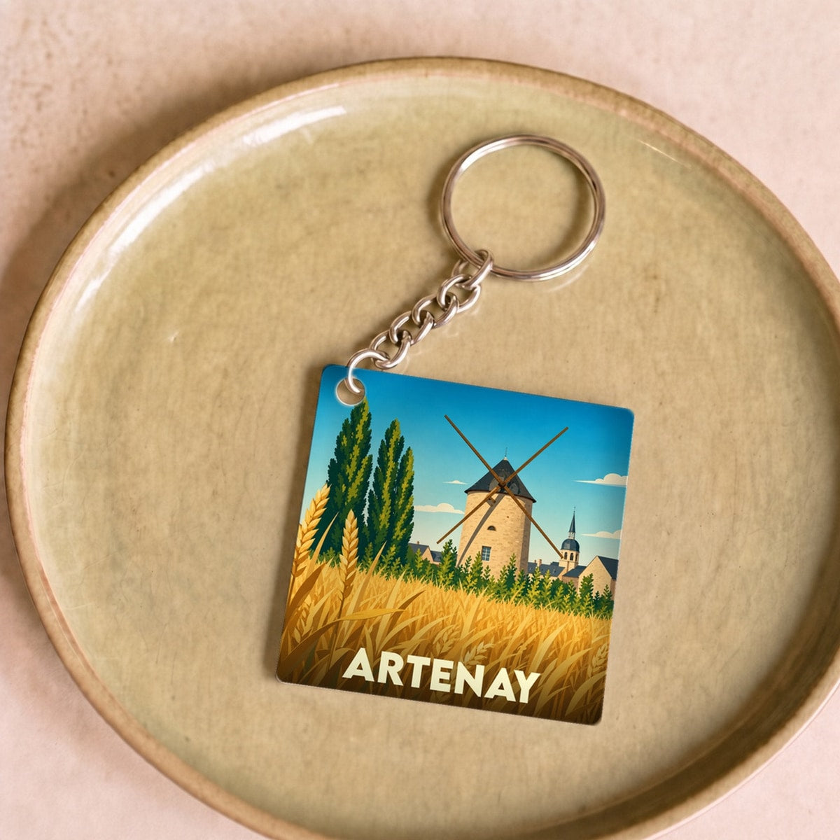 Porte-clés souvenir de la ville d'Artenay avec une illustration stylisée d'un moulin et d'un champ de blé.