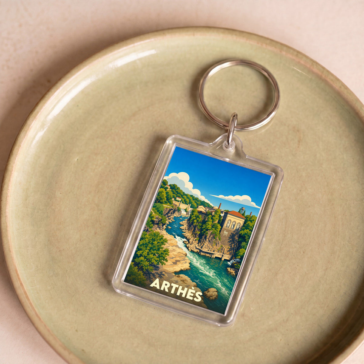 Porte-clés souvenir de la ville d'Arthès avec une illustration stylisée d'un paysage fluvial.