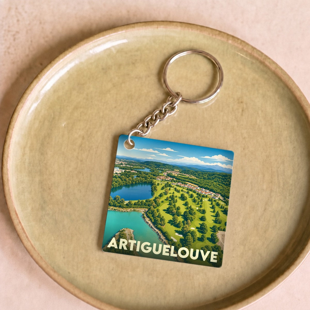 Porte-clés souvenir de la ville d'Artiguelouve avec une illustration stylisée de son paysage.