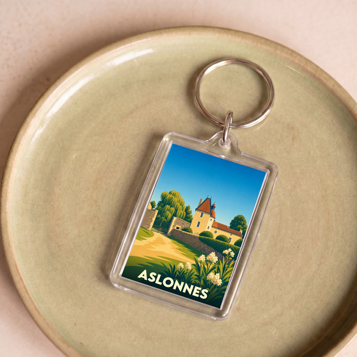 Porte-clés souvenir de la ville d'Aslonnes avec une illustration stylisée d'un manoir et de paysages verdoyants.
