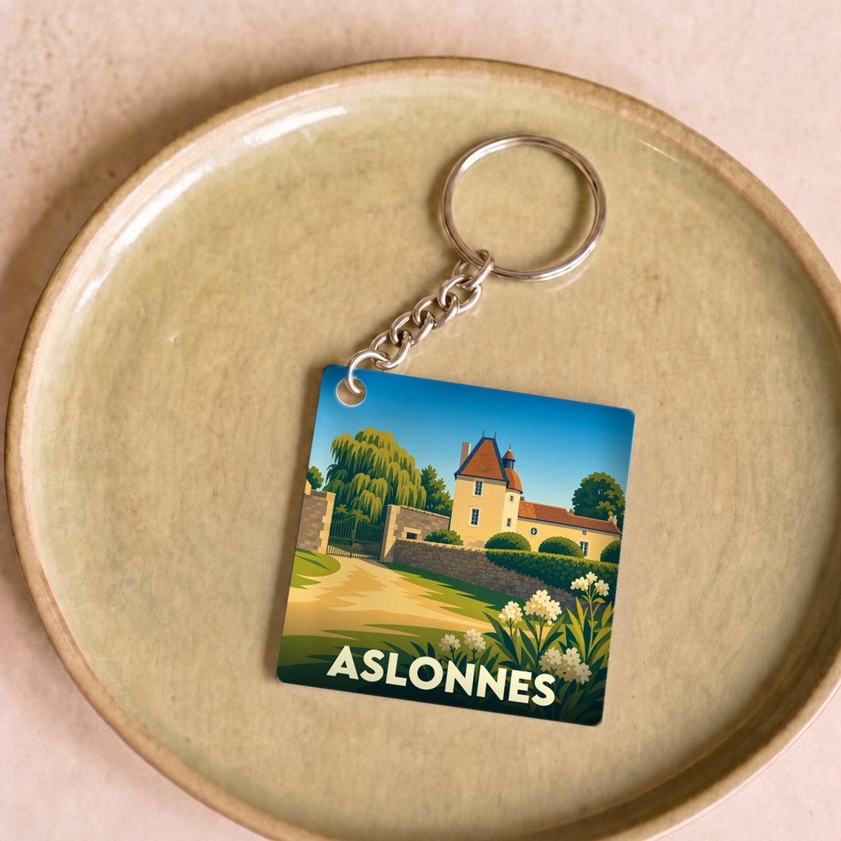 Porte-clés souvenir de la ville d'Aslonnes avec une illustration stylisée d'un manoir et de paysages verdoyants.