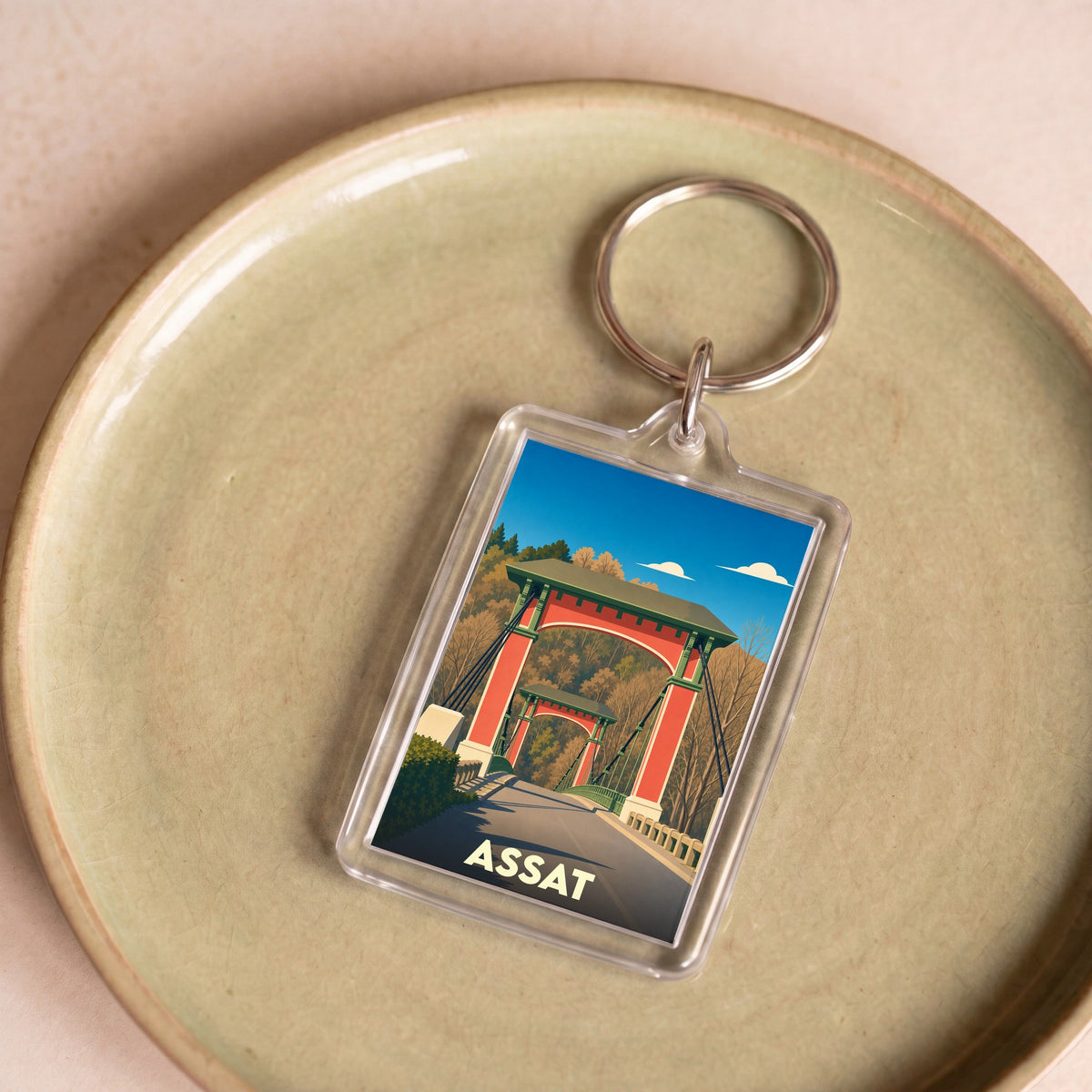 Porte-clés souvenir de la ville de Assat avec une illustration stylisée de son pont suspendu.