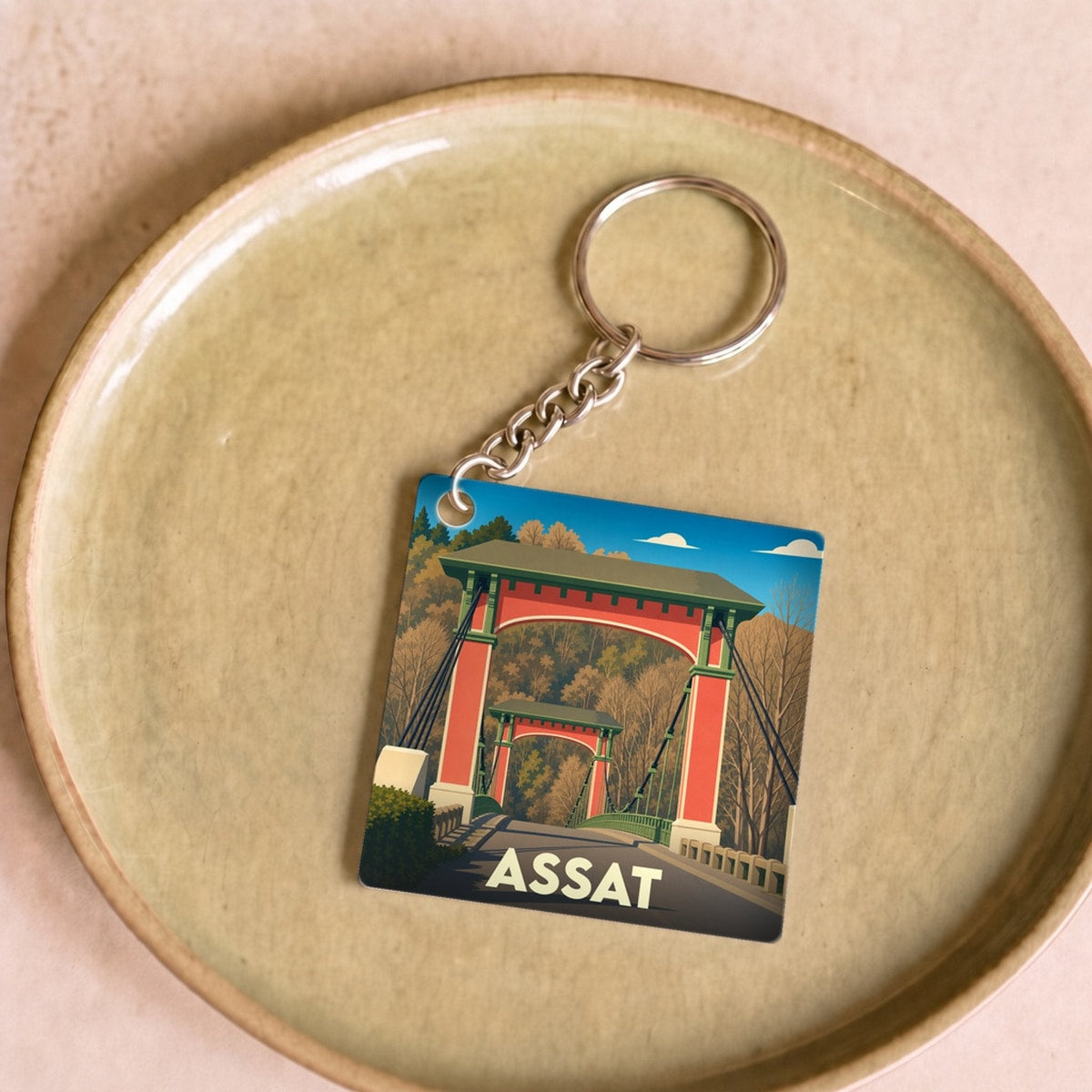 Porte-clés souvenir de la ville de Assat avec une illustration stylisée de son pont suspendu.