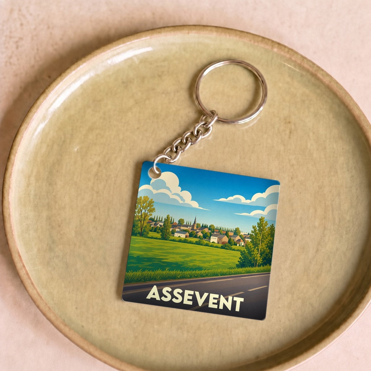 Porte-clés souvenir de la ville d'Assevent avec une illustration stylisée d'un paysage de campagne.