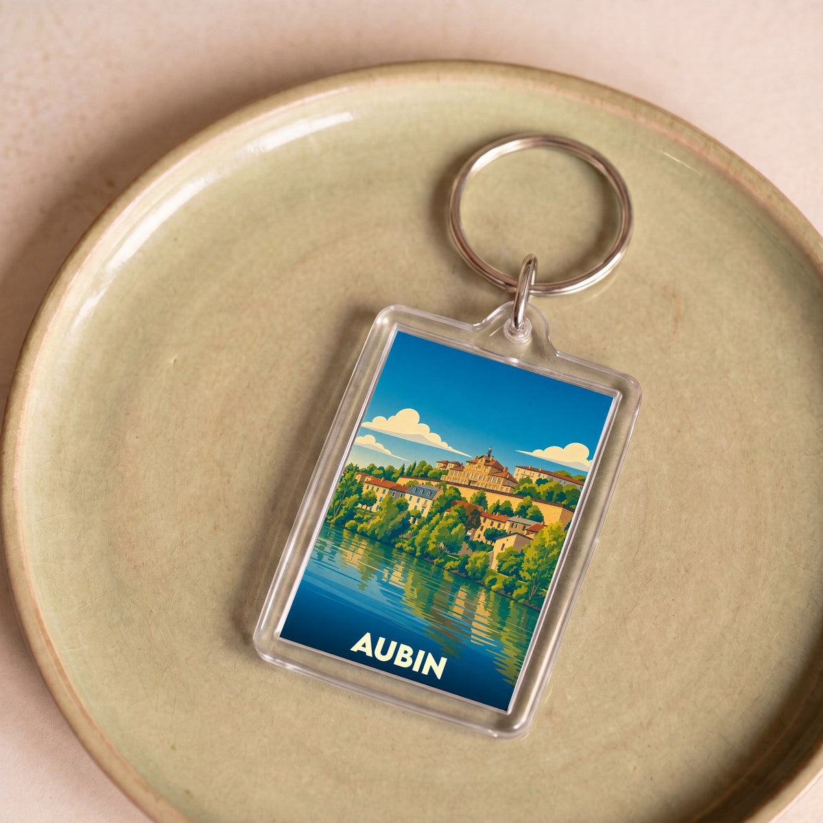 Porte-clés souvenir de la ville d'Aubin avec une illustration stylisée d'un paysage urbain au bord de l'eau.