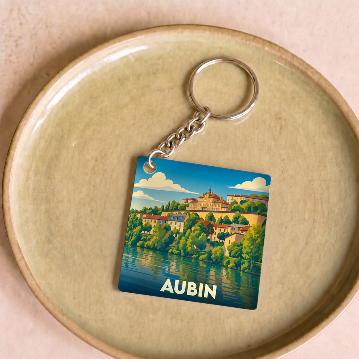 Porte-clés souvenir de la ville d'Aubin avec une illustration stylisée d'un paysage urbain au bord de l'eau.