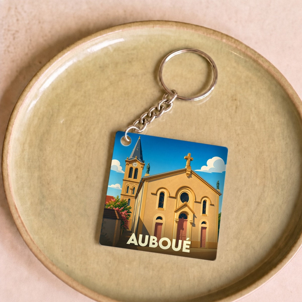 Porte-clés souvenir de la ville d'Auboué avec une illustration stylisée de son église sous un ciel bleu.