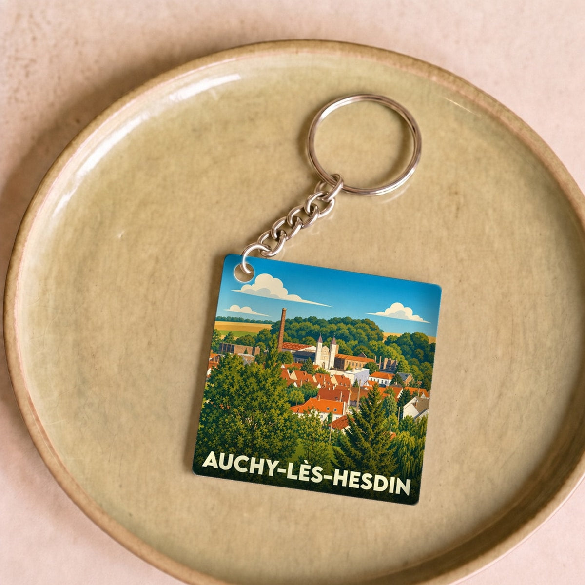 Porte-clés souvenir de la ville de Auchy-lès-Hesdin avec une illustration stylisée de son paysage urbain.