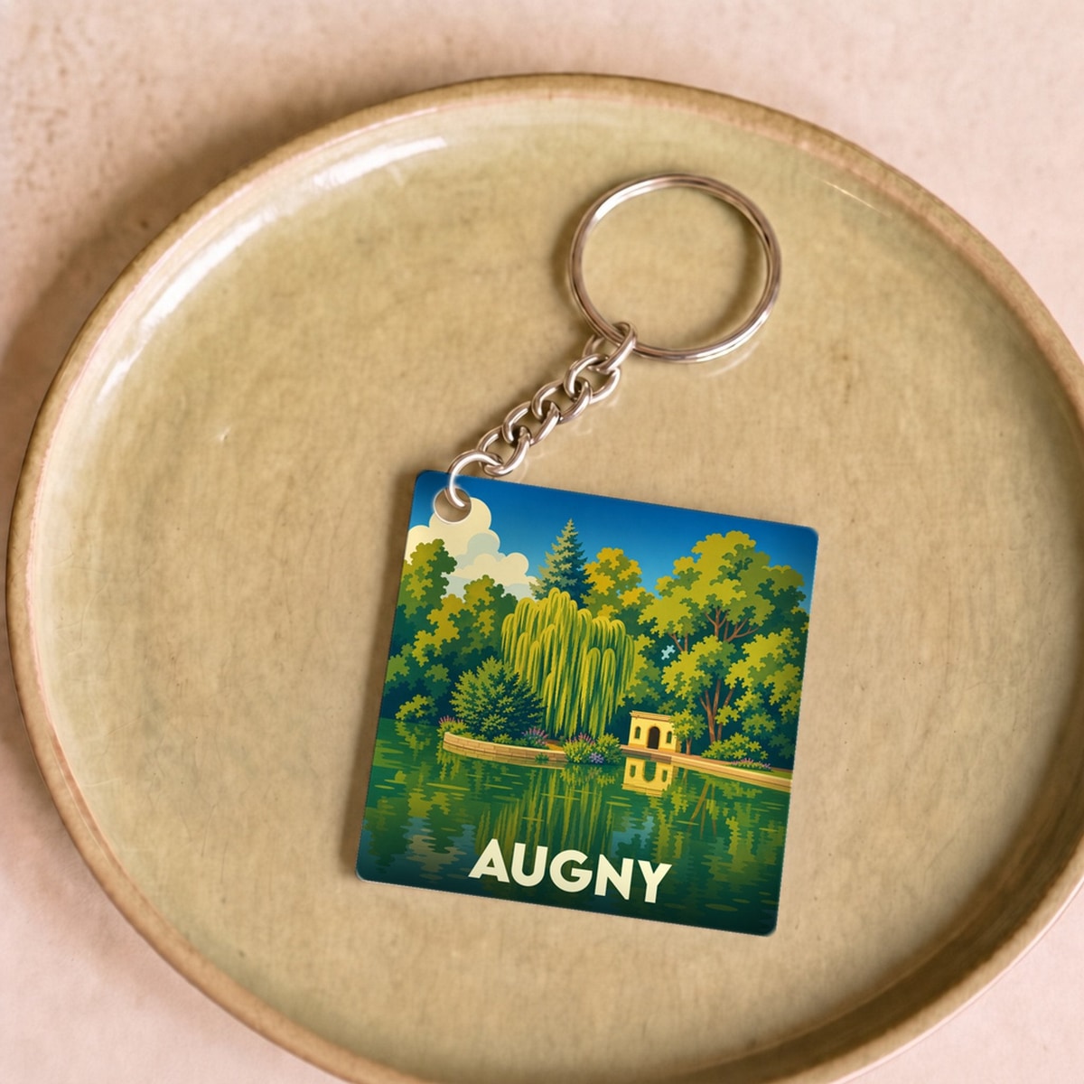 Porte-clés souvenir de la ville d'Augny avec une illustration stylisée d'un parc au bord de l'eau.