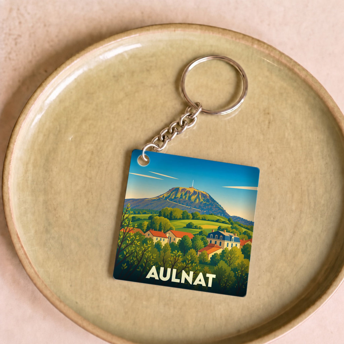 Porte-clés souvenir de la ville d'Aulnat avec une illustration stylisée d'un paysage de montagne.