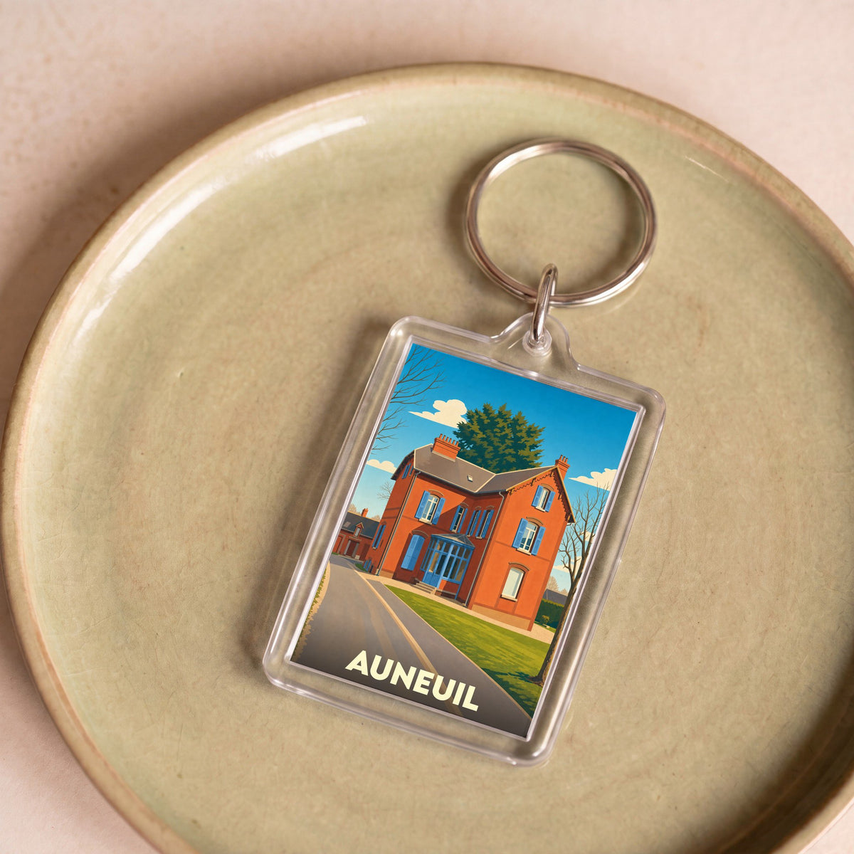 Porte-clés souvenir de la ville de Auneuil avec une illustration stylisée d'une maison traditionnelle.